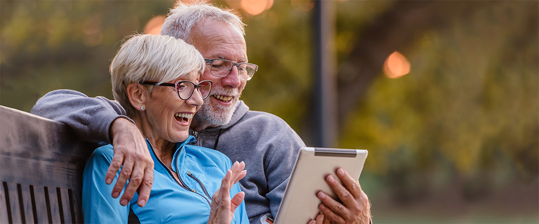 Couple seated outside looking at an iPad and smiling.